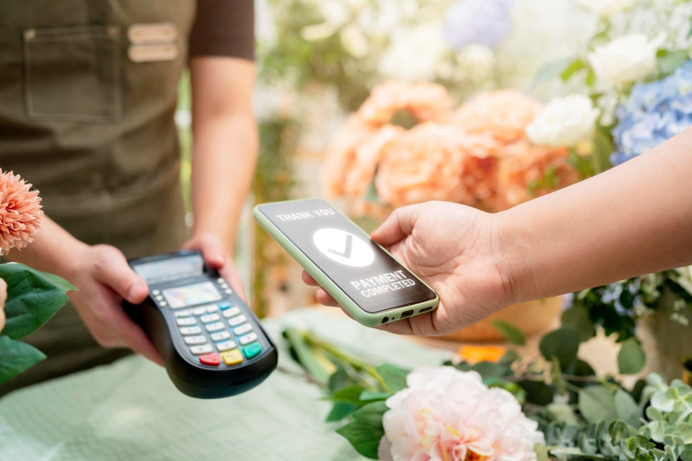 Person making a contactless payment with a smartphone at a flower shop.