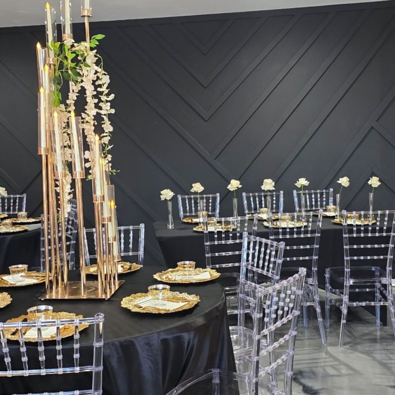 Elegant black and gold-themed event setup with tall bamboo centerpieces and clear chairs.